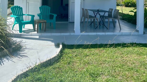 Un espace extérieur abrité, avec une table et des chaises, une porte portant l’inscription « Paradis » et un petit jardin.