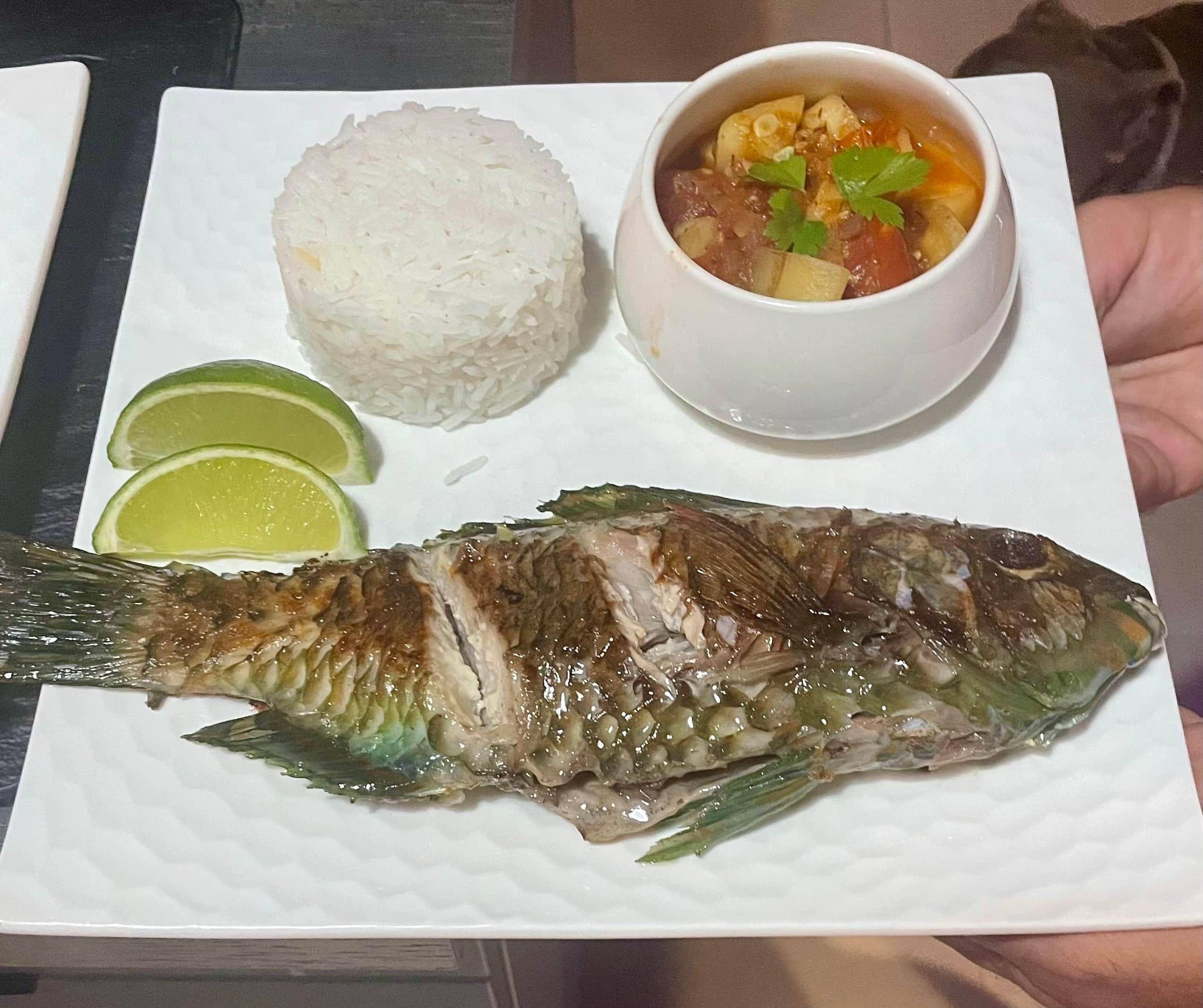 Un plato con un pescado entero, un tazón de sopa, una porción de arroz y cuñas de lima.
