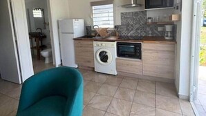 A compact kitchen with a washing machine, a microwave, and a sink. There is a teal chair in the foreground. - Gîte Coco-orchidées Le Domaine Mannou (Sainte Rose)