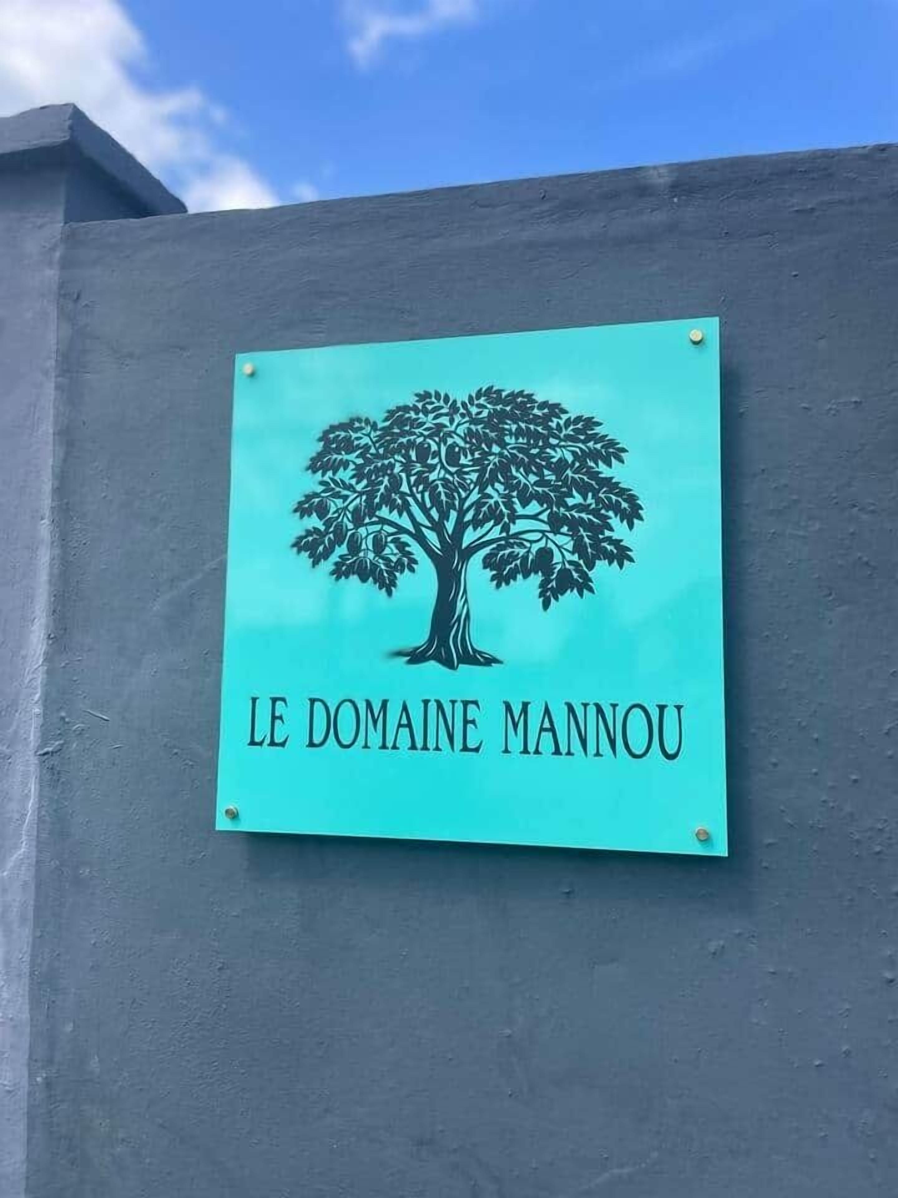 Un cartello con un albero e il testo "LE DOMAINE MANNOU" su sfondo color acquamarina.