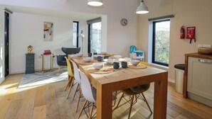 A modern kitchen with a wooden dining table, chairs, and pendant lights. There is a skylight above the table and a fire extinguisher on the wall. - 4 The Stoneyard (Bath)