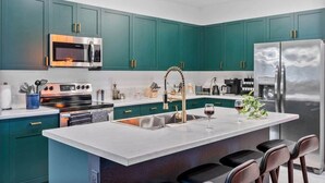 Una cocina moderna con armarios color turquesa, electrodomésticos de acero inoxidable y una isla central con taburetes de bar.