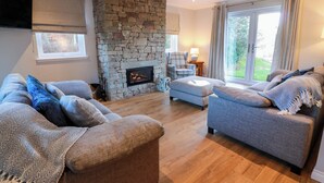 A living room with a stone fireplace, two sofas, a chair, and a large window with curtains. - Cramar Cottage (Glasgow)