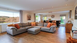 A spacious living room with a large sectional sofa, a dining area with wooden furniture, and a view of the outdoors. - Cramar Cottage (Glasgow)