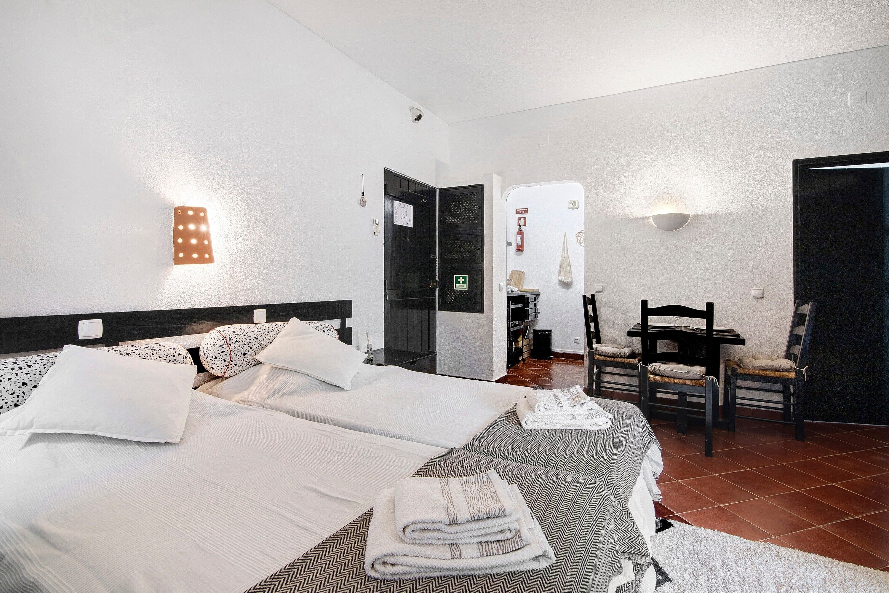 Habitación de hotel con dos camas, una mesa de comedor, sillas, una pequeña cocina y un baño con ducha.