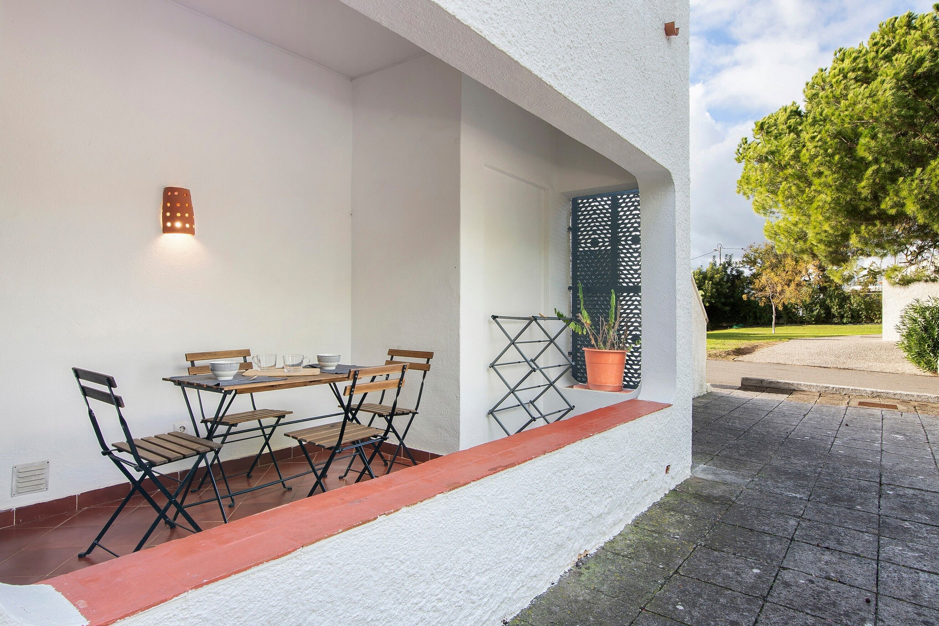 A patio with a table and chairs, a potted plant, and a door with a lattice design.