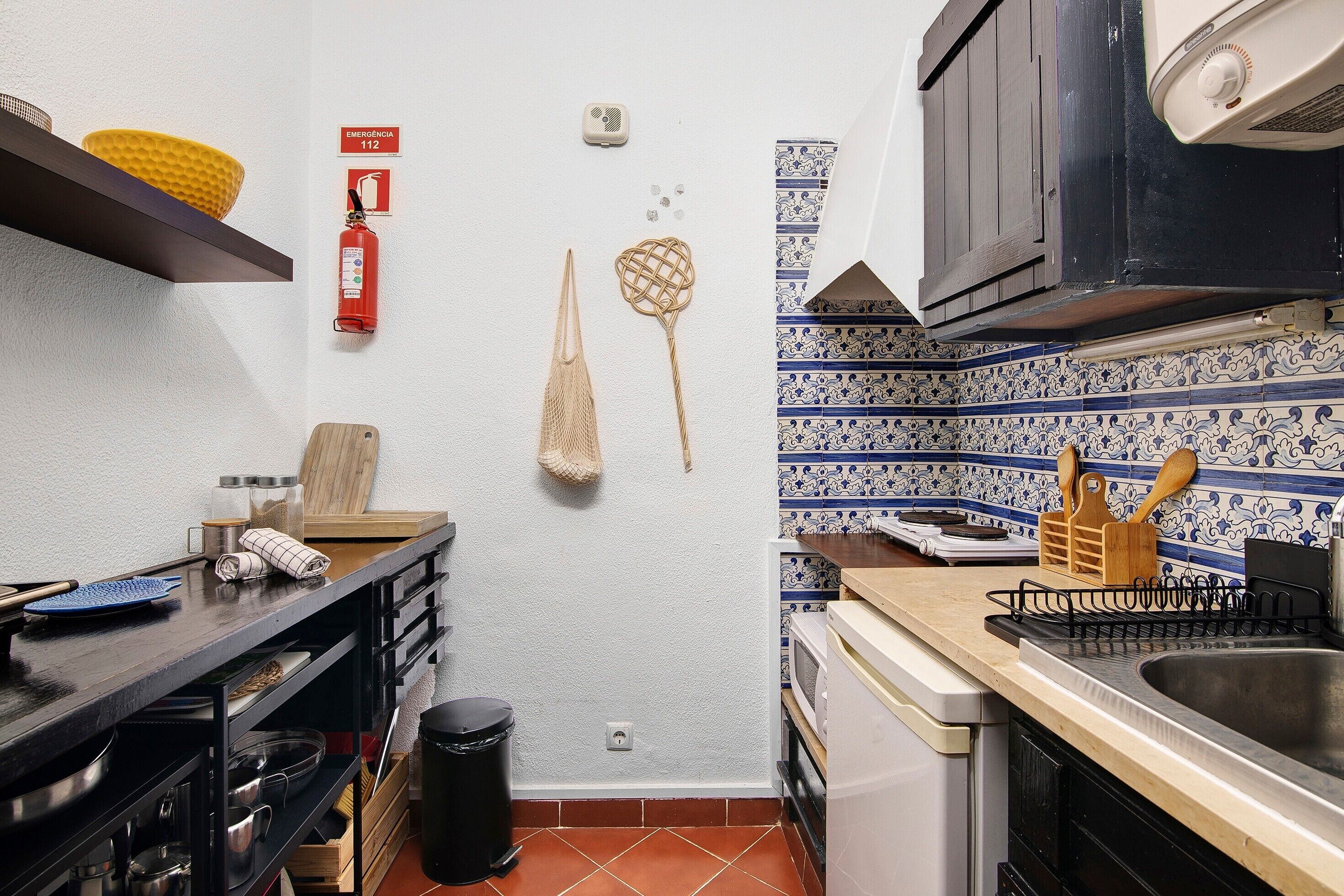 Une cuisine avec un mur recouvert de carreaux, un extincteur, un filet suspendu et une planche à découper en bois posée sur le comptoir.