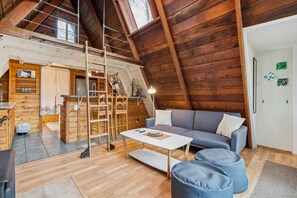 Ein gemütlicher Loftsitzung mit Holzwänden, einem Schlafplatz in der Mansarde, einer Couch und einem Couchtisch.