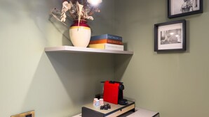 A room with a shelf holding books and a vase with dried flowers, a coffee machine, and a framed picture on the wall. - GuestHost - In the heart of Brera, in a 20th-century Art Nouveau building on the 1st floor with elevator is the newly renovated double room with large bathroom, a cozy double bed, air conditioning, wifi, mini-bar, coffee maker, smart TV, bath linens, ill (Milan)