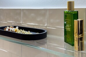 A bathroom with a glass shelf, a green bottle of Rabarbaro perfume, and a gold-colored object. - GuestHost - In the heart of Brera, in a 20th-century Art Nouveau building on the 1st floor with elevator is the newly renovated double room with large bathroom, a cozy double bed, air conditioning, wifi, mini-bar, coffee maker, smart TV, bath linens, ill (Milan)