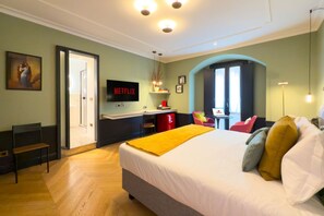 A hotel room with a bed, a desk with a computer, a chair, a TV, and a door leading to a bathroom.