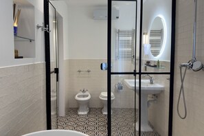 A modern bathroom with a glass partition, two toilets, a sink, and a shower.