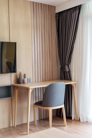 A modern room with a wooden desk, a chair, a television mounted on the wall, and a window with curtains. - Beachfront 1524 Wyndham Gardens Condo Naithon (Sa Khu)