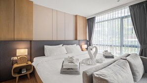 A hotel room with a large bed, a bedside table with a lamp, a chair, and a view of the outdoors through large windows. - Beachfront 1524 Wyndham Gardens Condo Naithon (Sa Khu)