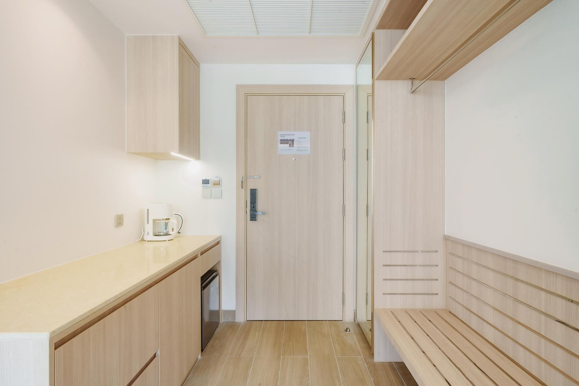 A narrow hallway with a kitchenette on the left, a door with a sign, and a bench on the right.