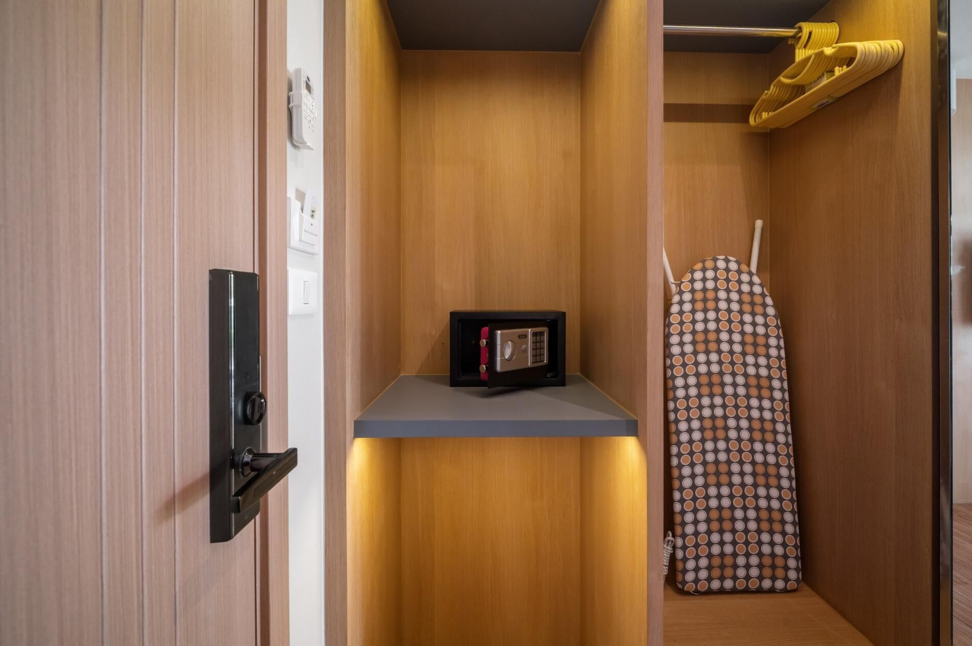 Una habitación compacta con un armario de madera, una caja fuerte pequeña y una tabla de planchar estampada.