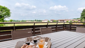 Ein Tisch mit einer Platte Croissants, Kaffee und Saft auf einer Terrasse mit Blick auf Gebäude und Grünflächen.