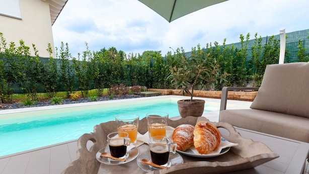 Ein Tablett mit Getränken und Gebäck auf einer Terrasse, im Hintergrund ein Pool und viel Grün.