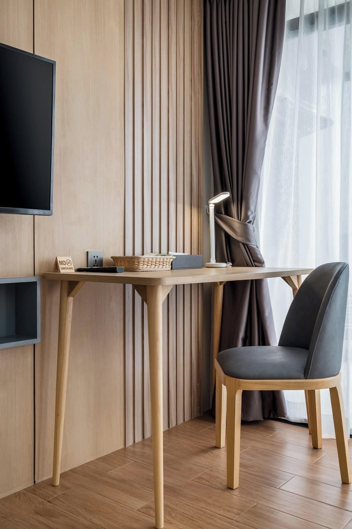 A modern room with a wooden desk, a chair, a desk lamp, and a television mounted on the wall.