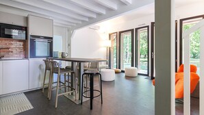 A modern kitchen with a built-in oven, a dining area with bar stools, and a bright living space with a large window.