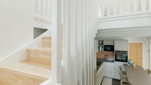 A modern kitchen with a dining area, wooden staircase, and a view of the living area.