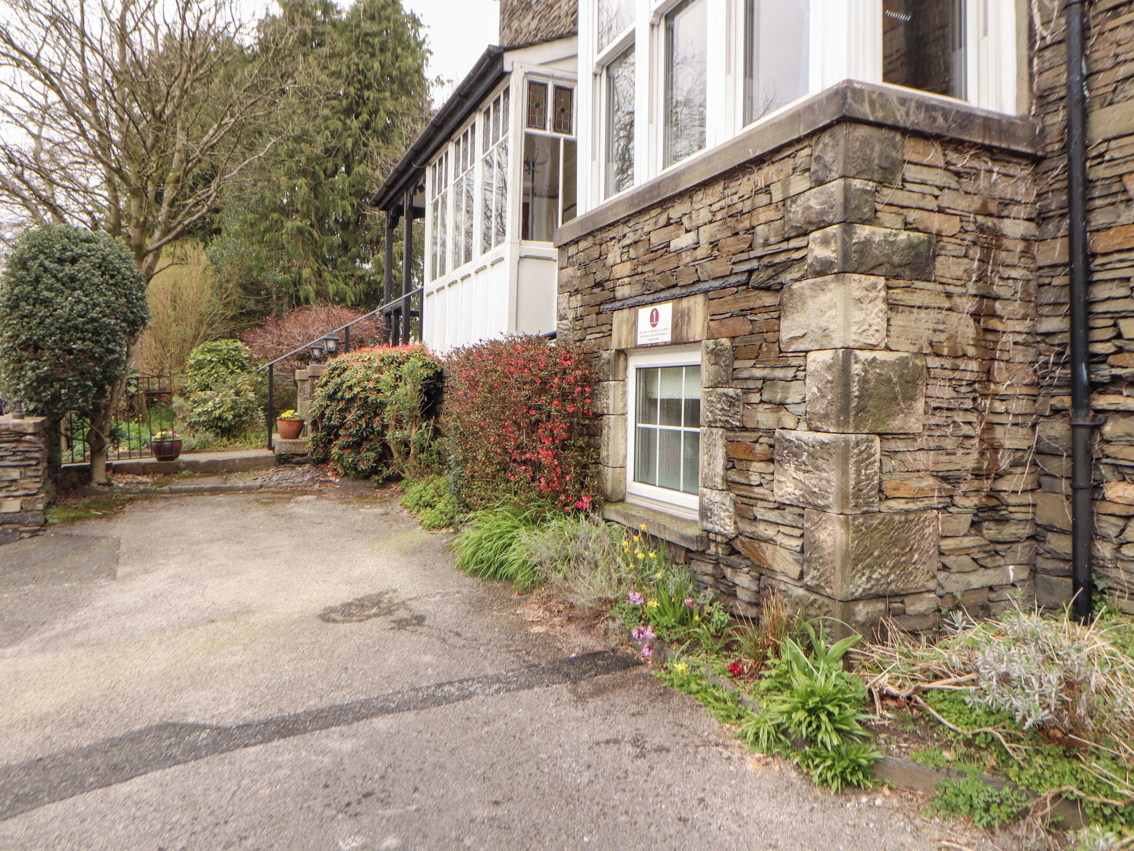 A stone building with a paved driveway, a window with a sign, and various plants.