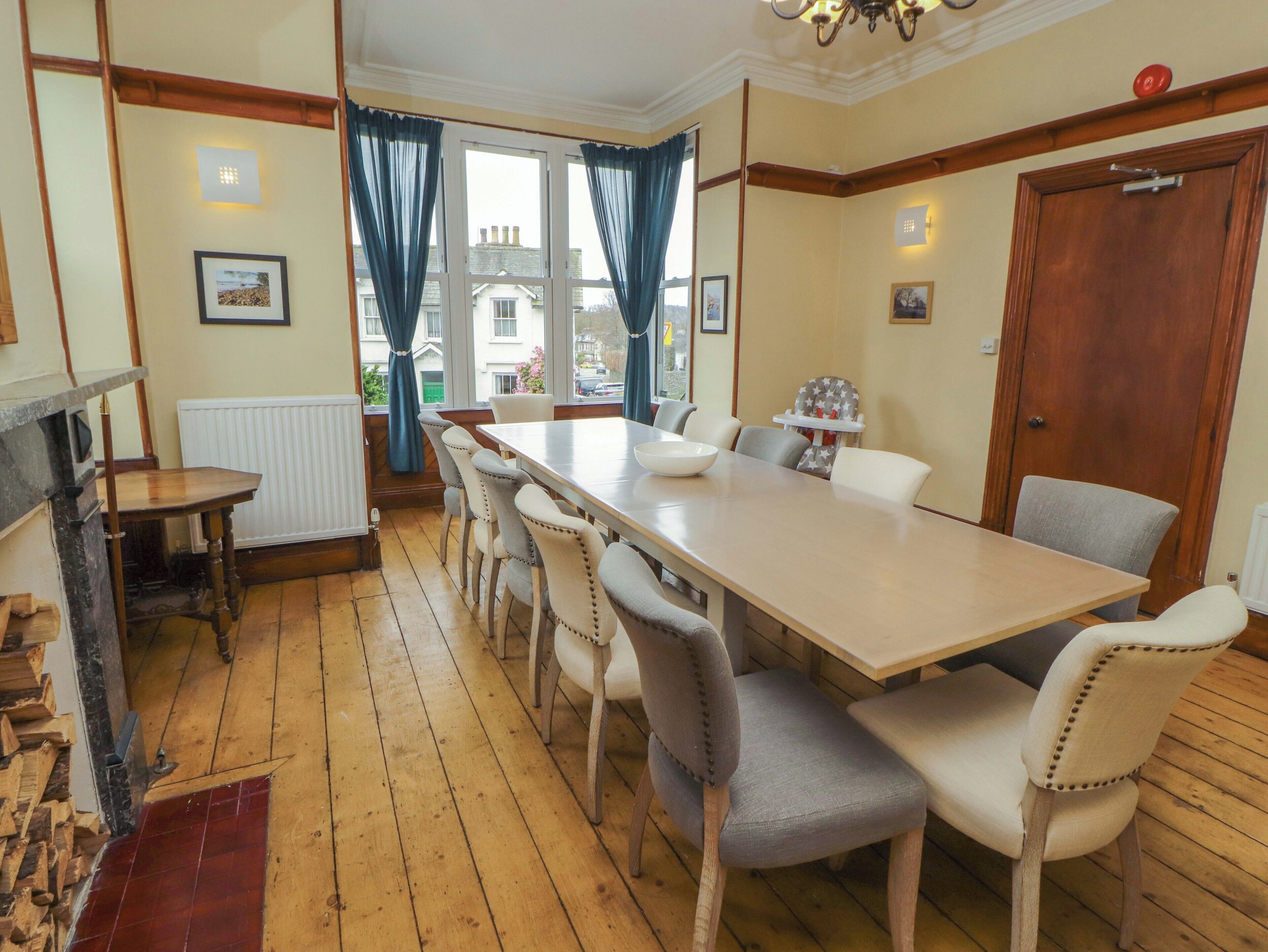 A dining room with a long table, chairs, a fireplace, and a view through the window.