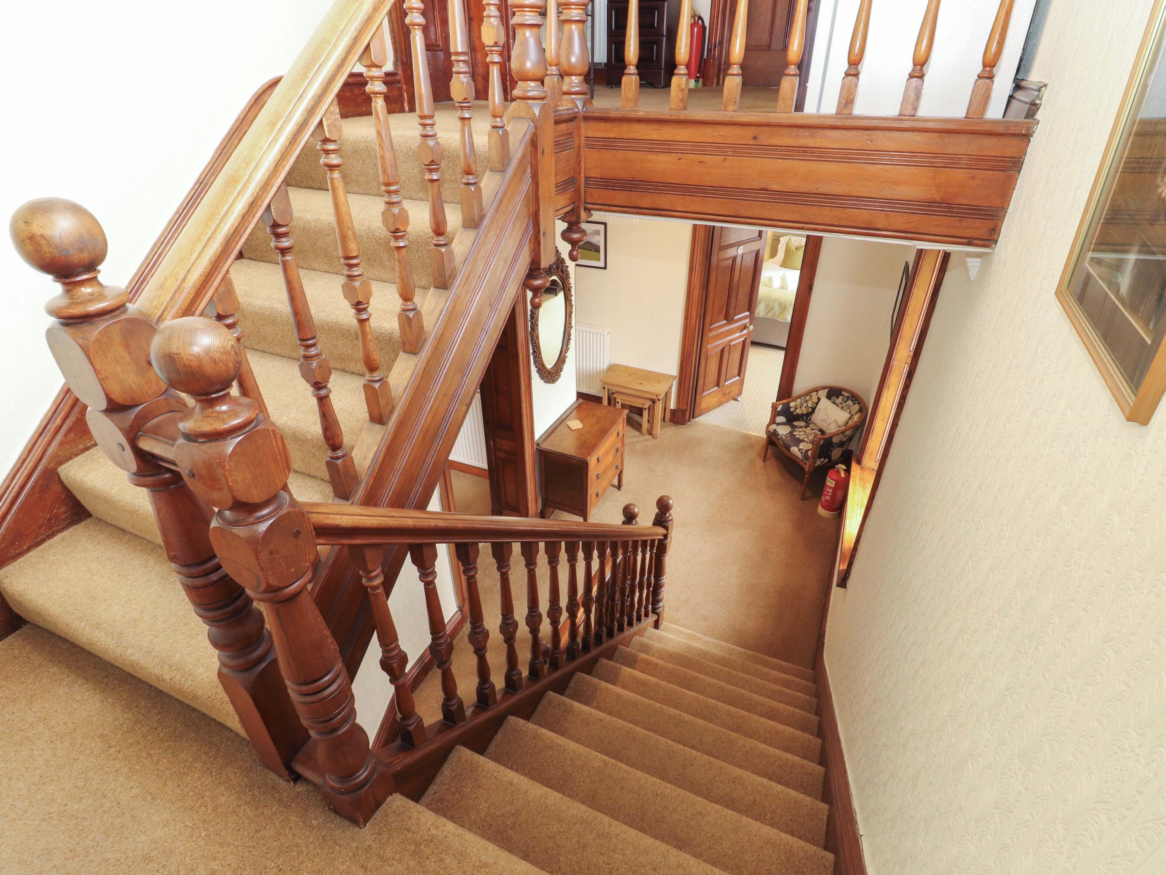 A wooden staircase with a handrail, carpeted steps, and a chair in the background.