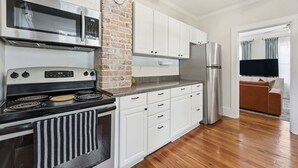 A modern kitchen with white cabinets, a brick accent wall, stainless steel appliances, and a wooden floor. - The Pearl Unit A, Stay for 4 (St. Augustine)