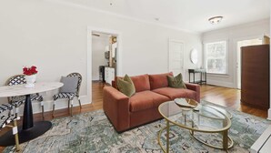 A living room with a brown sofa, a glass coffee table, a patterned rug, and a ceiling fan. - The Pearl Unit A, Stay for 4 (St. Augustine)