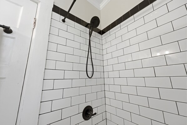 Une douche avec des carreaux blancs et noirs, une pomme de douche noire et un tuyau noir.
