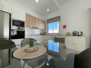 Une cuisine moderne avec une table à manger en verre, des appareils électroménagers en acier inoxydable et une fenêtre offrant une vue agréable.