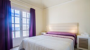 Ein Schlafzimmer mit einem Bett, einem Nachttisch, einer Nachttischlampe und einem Fenster mit Vorhängen.