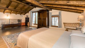 Ein Schlafzimmer mit Holzboden, einem Bett, einem Nachttisch, einer Lampe, einer Kommode und einem Fenster mit Vorhängen.