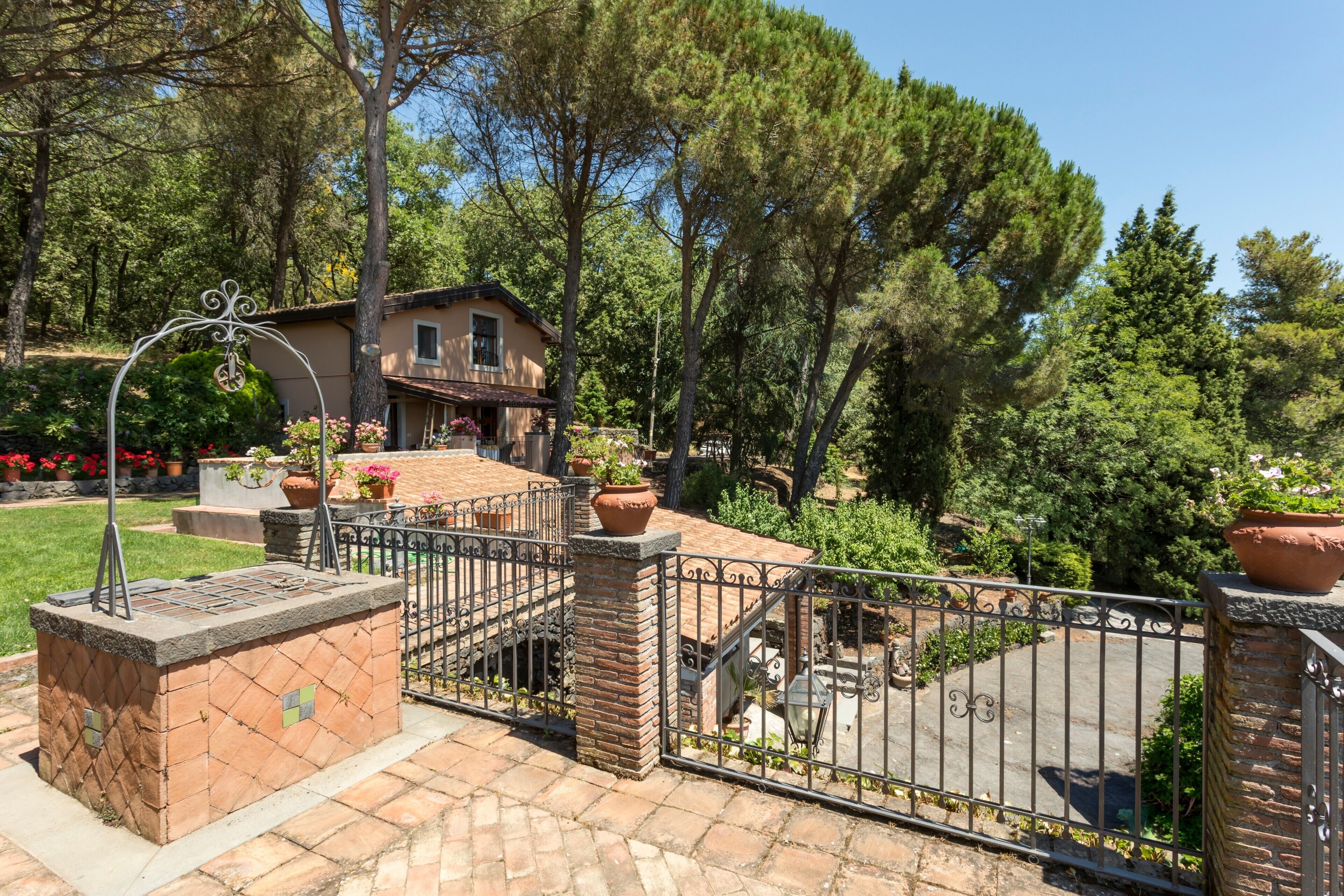 A brick outdoor area with a metal gate, potted plants, and a building with a balcony.