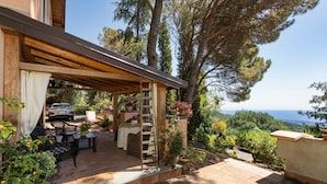Ein überdachter Patio-Bereich mit Gartenmöbeln, ein geparktes Auto und Meerblick.