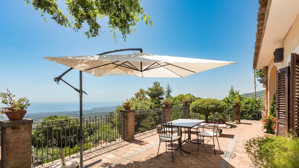 A patio with a table and chairs, a large umbrella, and a view of the landscape.