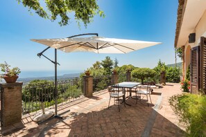 Een terras met een tafel, stoelen en een grote parasol, met uitzicht op het landschap.