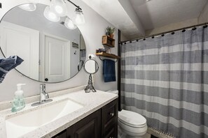 Un baño con un lavamanos blanco, un espejo, un perchero para toallas y una cortina de ducha.