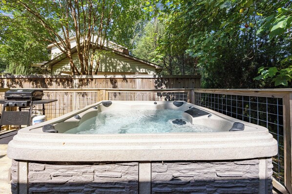 Un jacuzzi en un patio trasero con valla de madera y árboles al fondo.