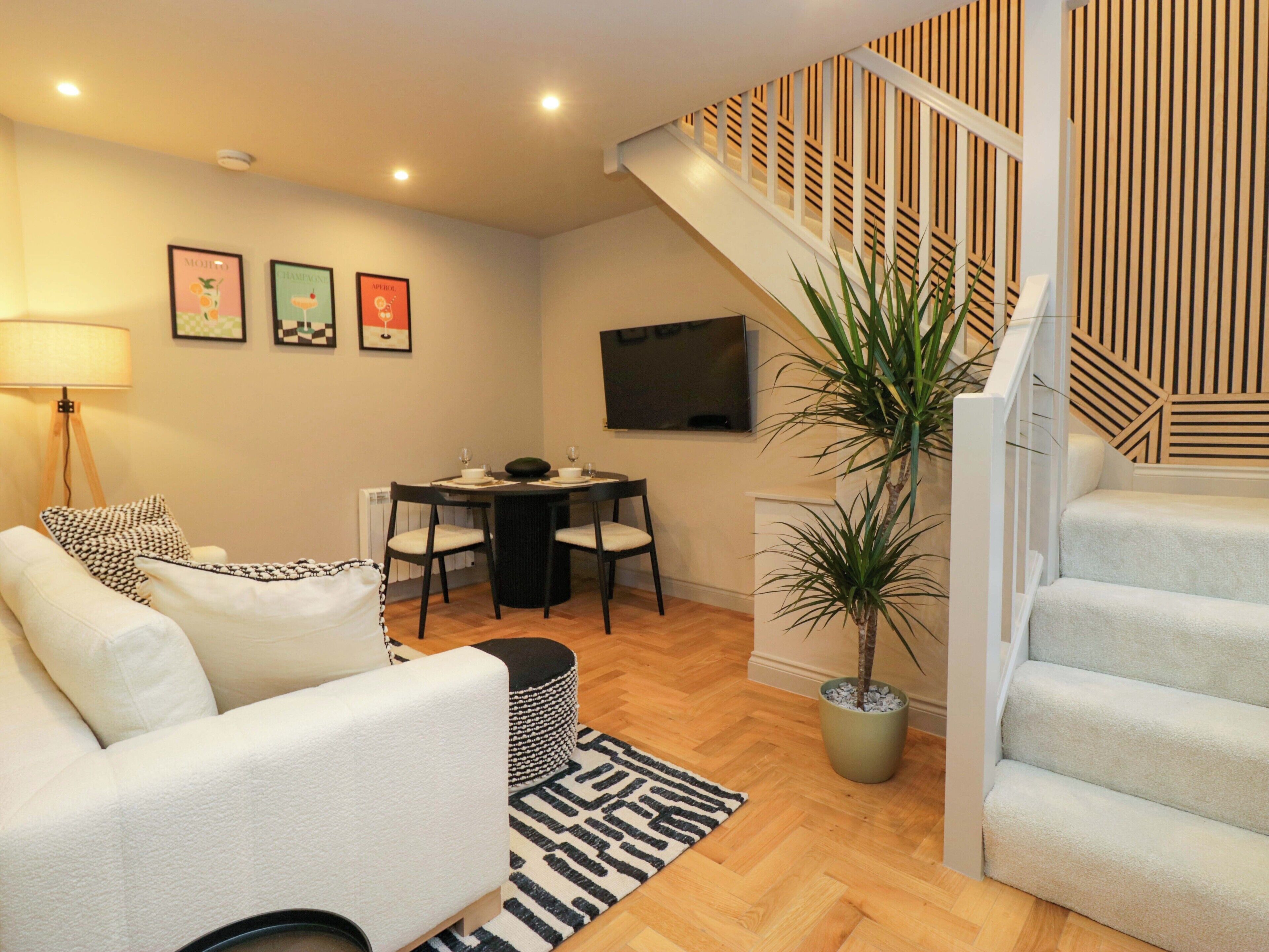 A modern living room with a sofa, dining table, chairs, a TV, and a staircase with a geometric railing.