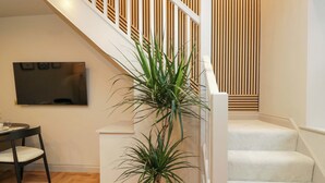 Un escalier avec une rampe blanche, une plante en pot et un téléviseur à écran plat fixé au mur.