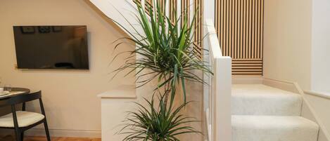 A staircase with a white railing, a potted plant, and a flat-screen TV mounted on the wall.
