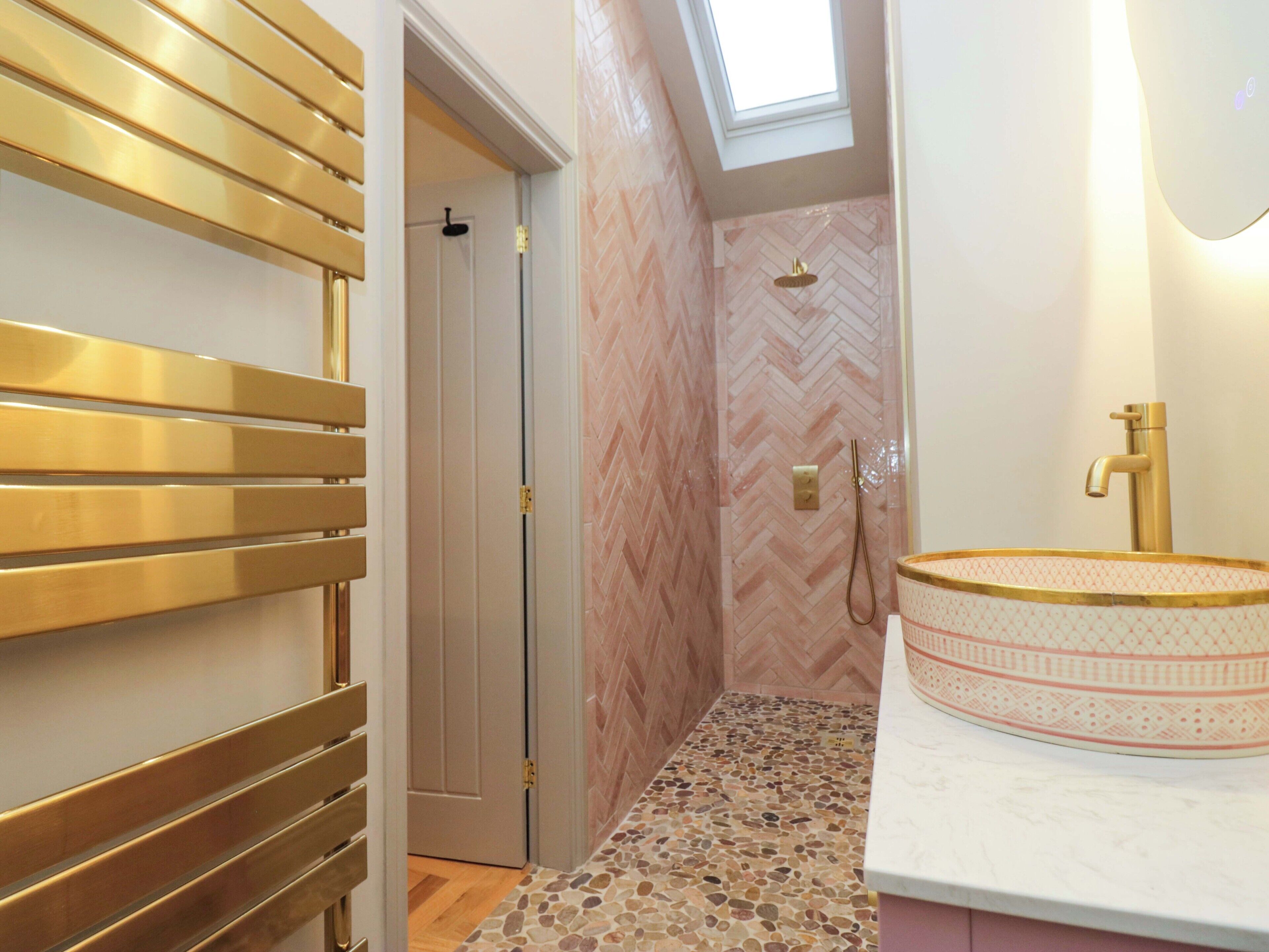 A bathroom with a herringbone-patterned wall, a shower with a gold faucet, and a mosaic-tiled floor.