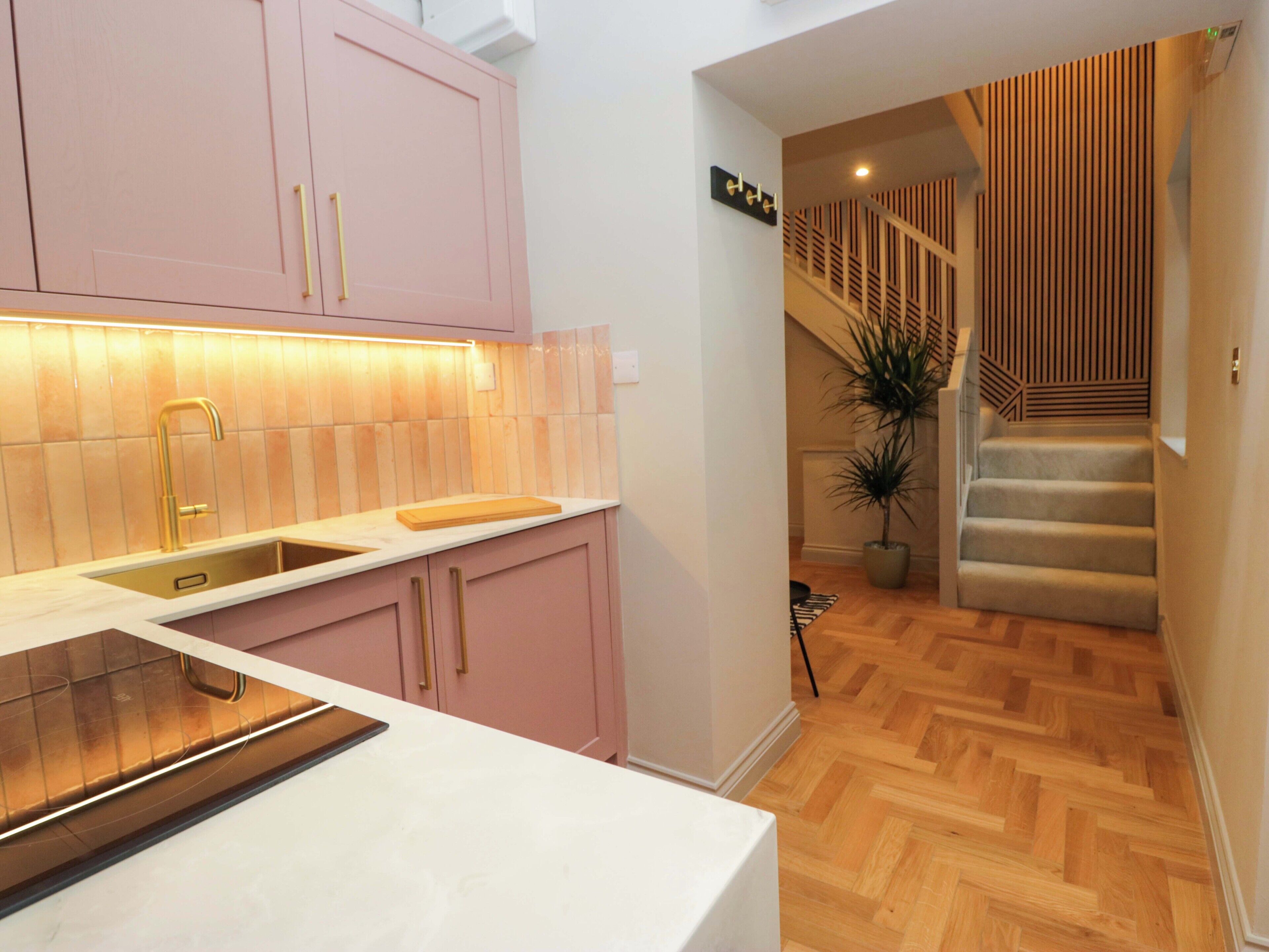 A modern kitchen with pink cabinets, a white countertop, and a wooden cutting board.