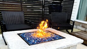 Una mesa de piedra con hogar en el centro, rodeada de sillas de metal negro.