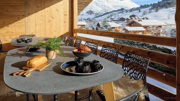Una baita di legno con un tavolo rotondo apparecchiato per la colazione, con vista su un paesaggio montano innevato.