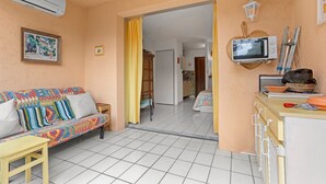 A living room with a sofa, a small table, an air conditioner, a framed picture, and a doorway leading to another room.