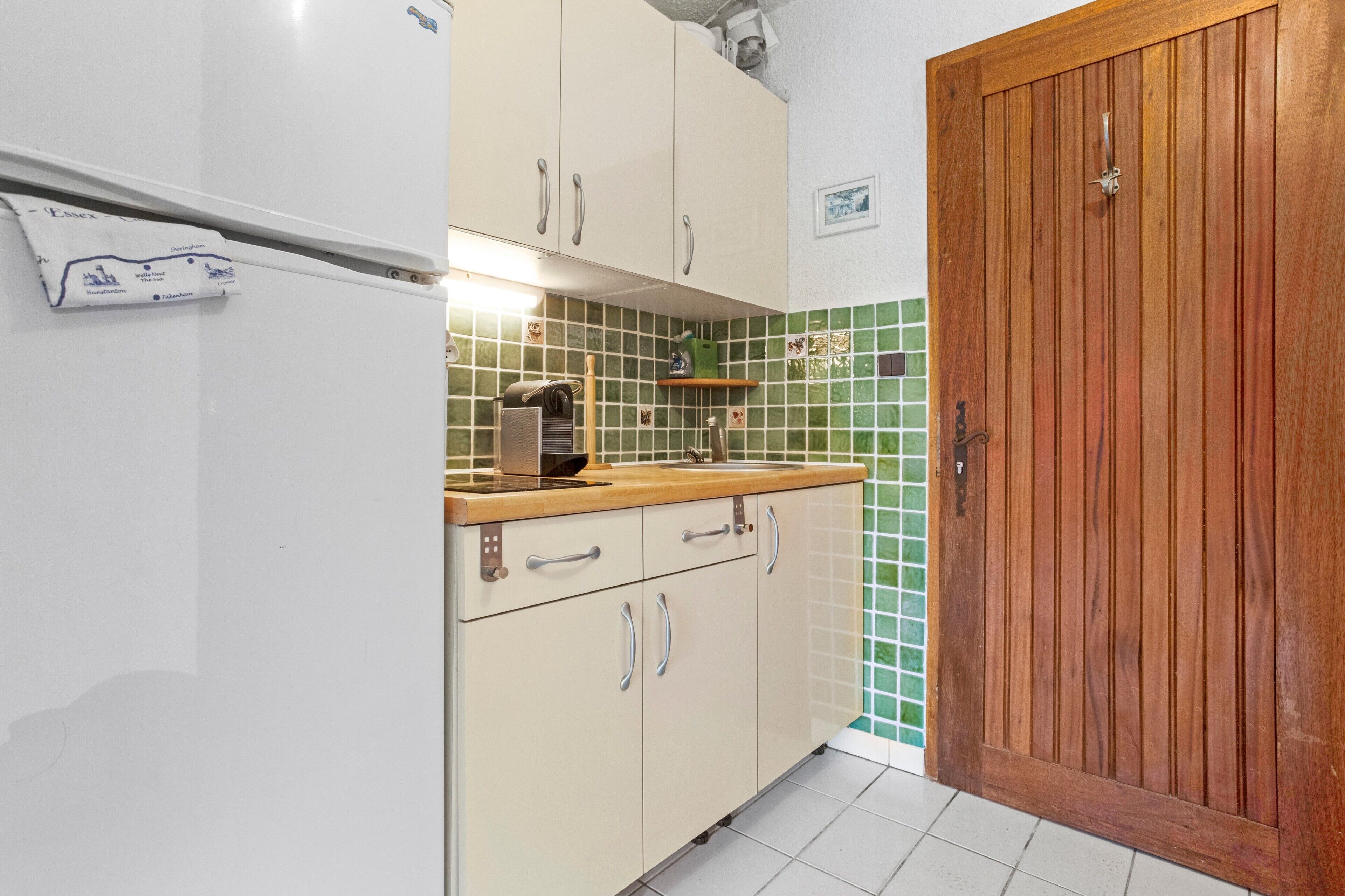 Une cuisine avec des armoires blanches, une porte en bois et un dosseret de carrelage vert.