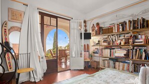 Een kamer met een bed, een boekenkast, een stoel en uitzicht op het groen.